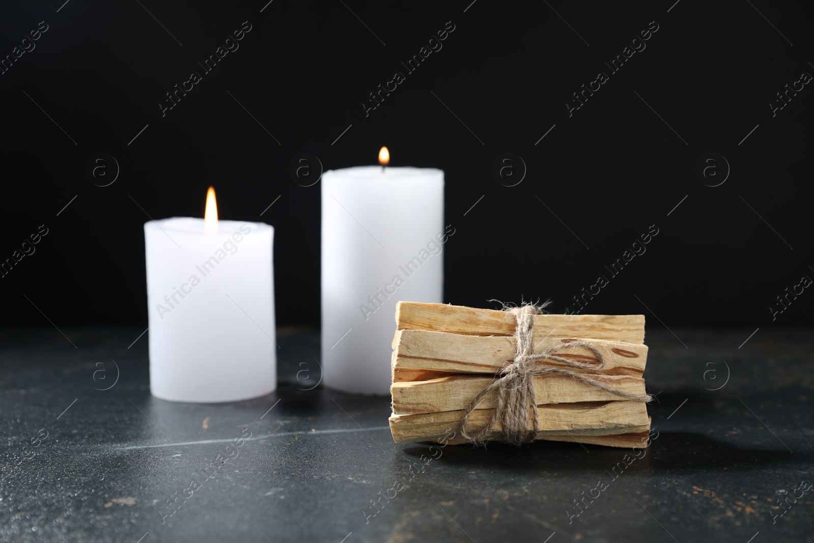 Photo of Bunch of palo santo sticks and burning candles on dark table