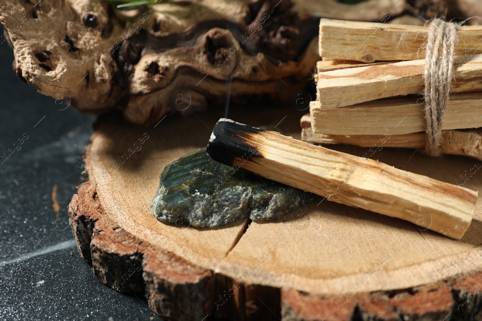 Photo of Smoldering palo santo stick, gemstone and snag on dark table, closeup