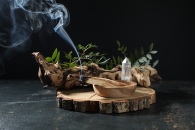 Photo of Smoldering palo santo stick, gemstone, snag and green branch on dark table