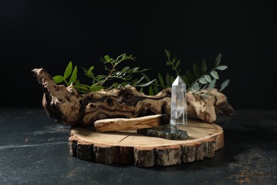 Photo of Burnt palo santo stick, gemstones, snag and green branch on dark table