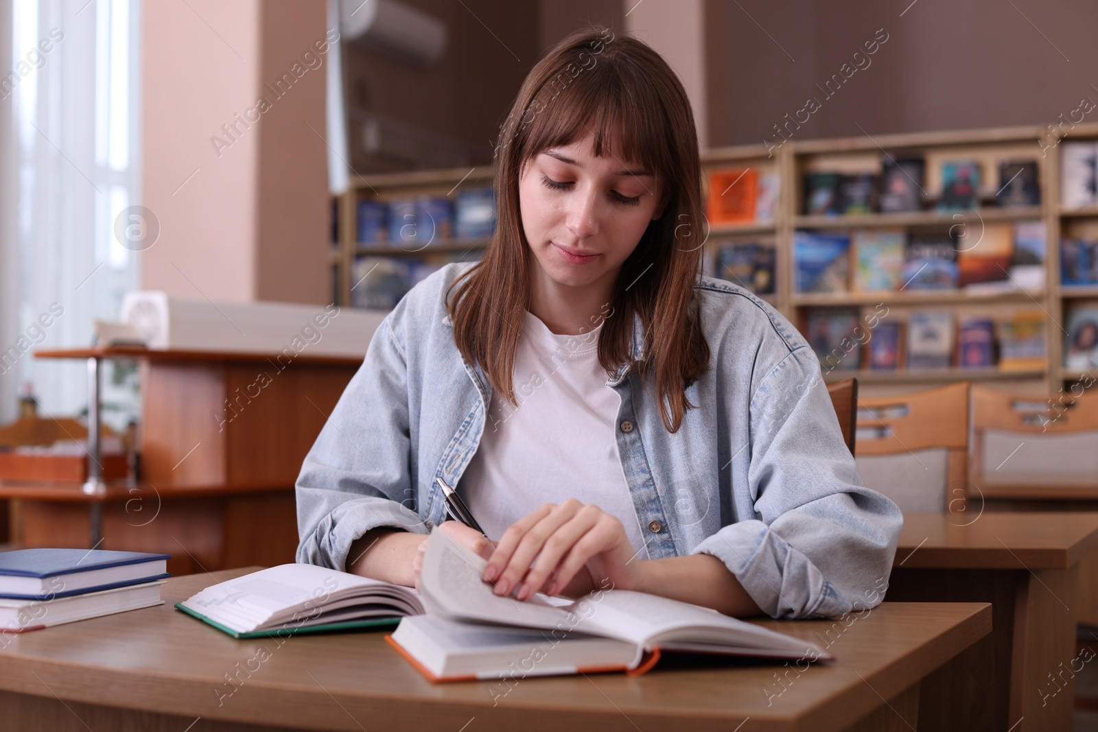 Photo of Beautiful woman reading book and taking notes at desk in public library