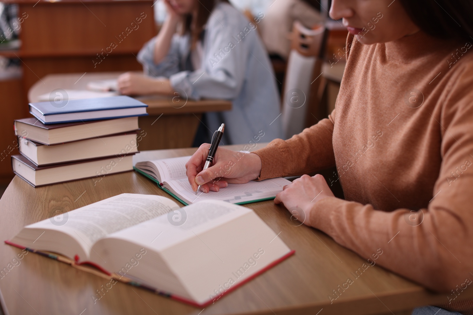 Photo of Woman reading book and taking notes at desk in library, closeup