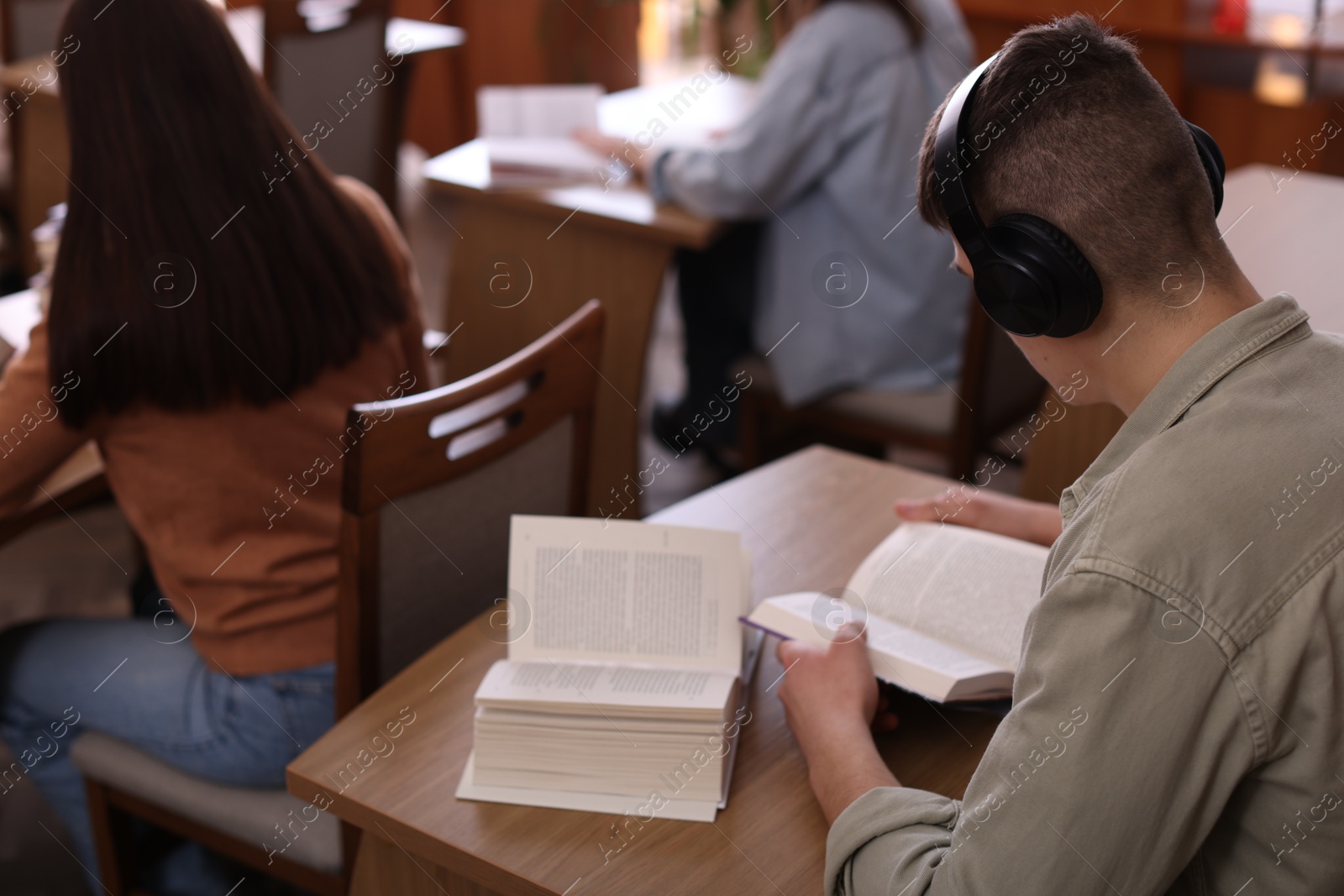 Photo of Man in headphones reading books at desk in public library