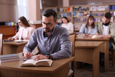 Photo of Handsome man reading book and taking notes at desk in public library