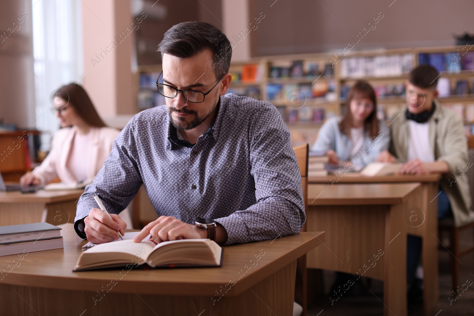 Photo of Handsome man reading book and taking notes at desk in public library