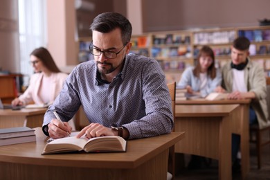 Photo of Handsome man reading book and taking notes at desk in public library