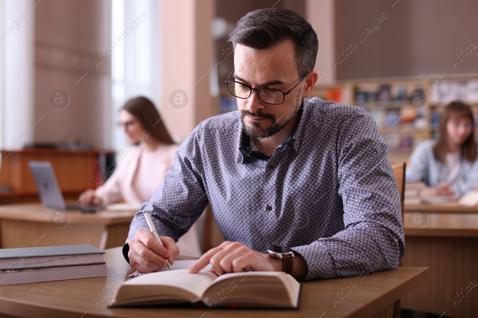 Photo of Handsome man reading book and taking notes at desk in public library