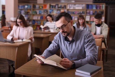 Photo of Handsome man reading book at desk in public library