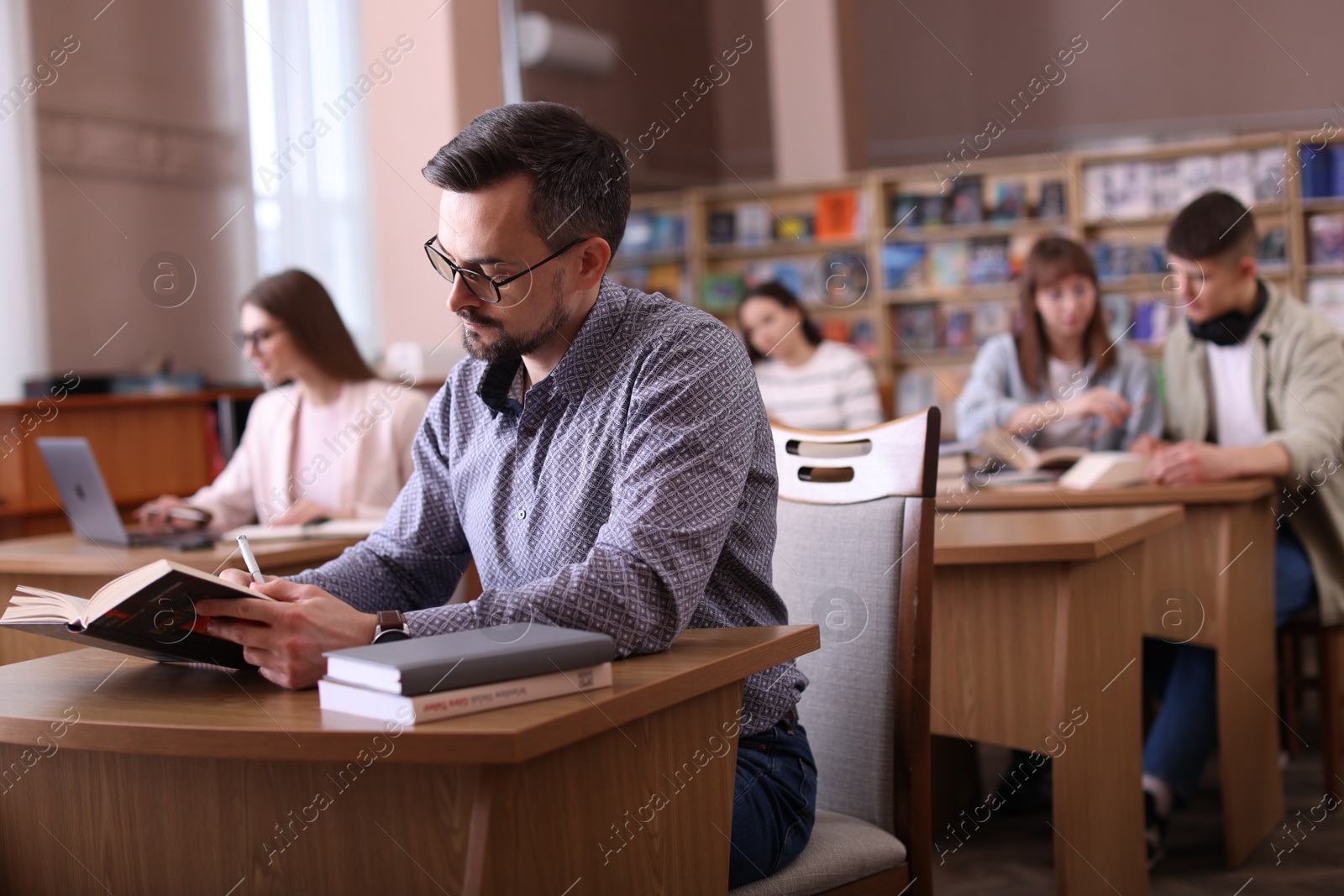 Photo of Handsome man reading book and taking notes at desk in public library