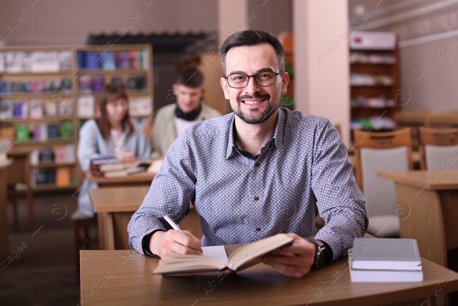 Photo of Portrait of smiling man with book at desk in public library