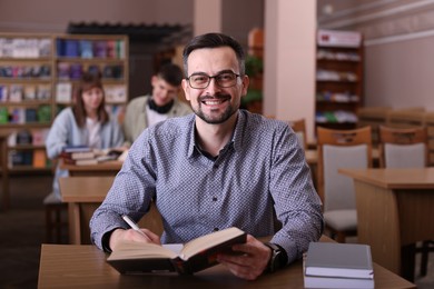 Photo of Portrait of smiling man with book at desk in public library