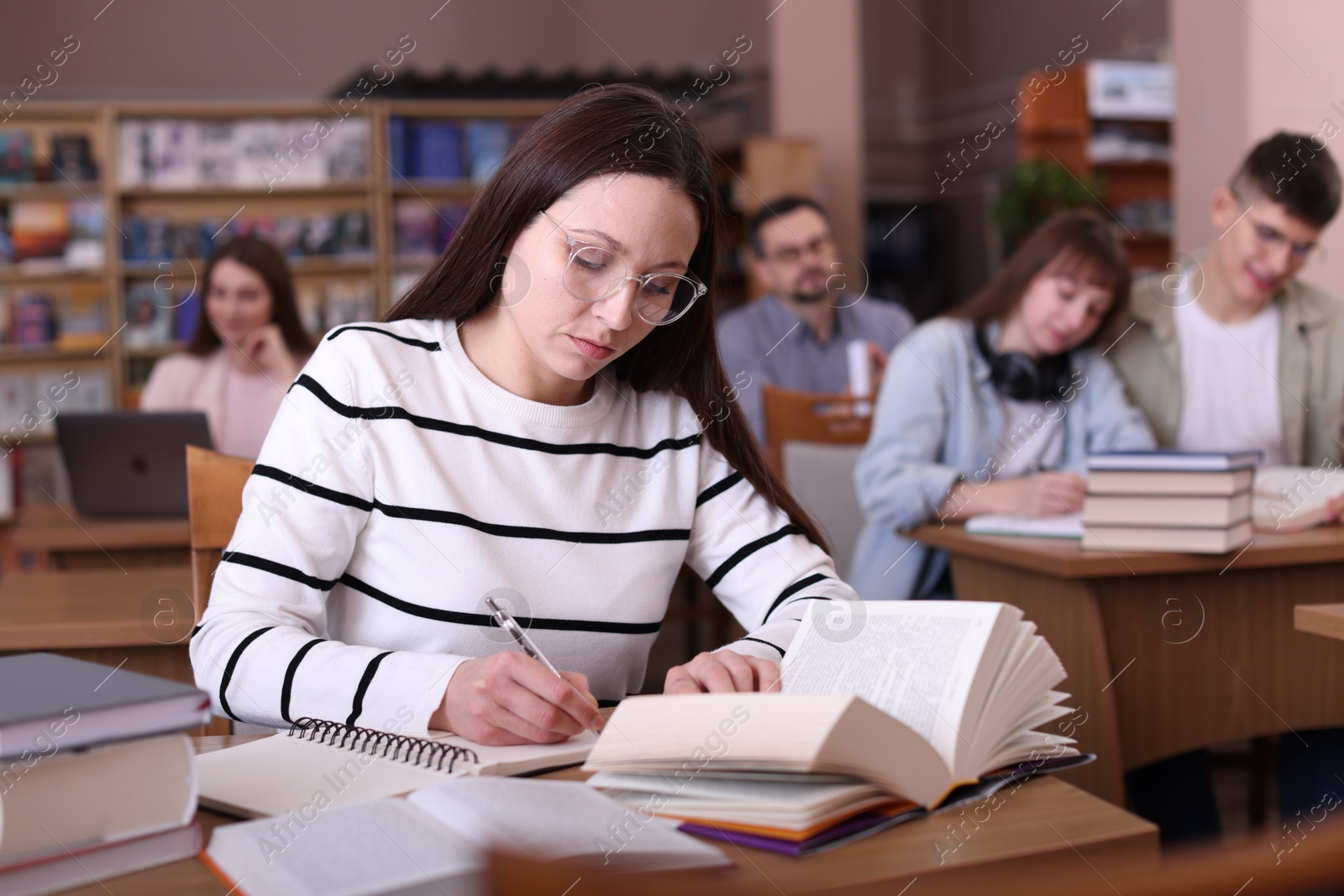 Photo of Beautiful woman reading book and taking notes at desk in public library