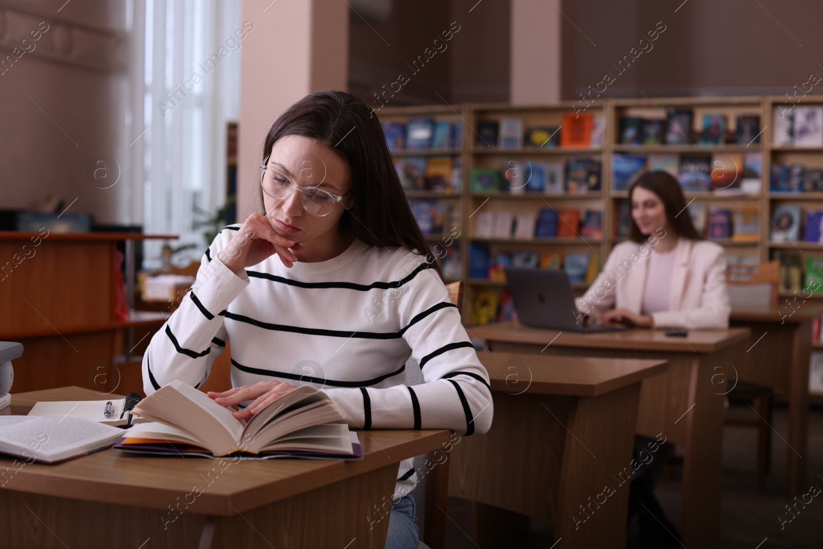 Photo of Beautiful woman reading book at desk in public library