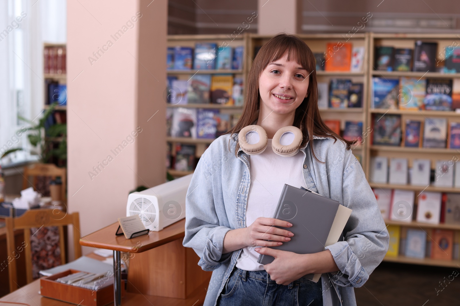 Photo of Portrait of smiling woman with books in library. Space for text