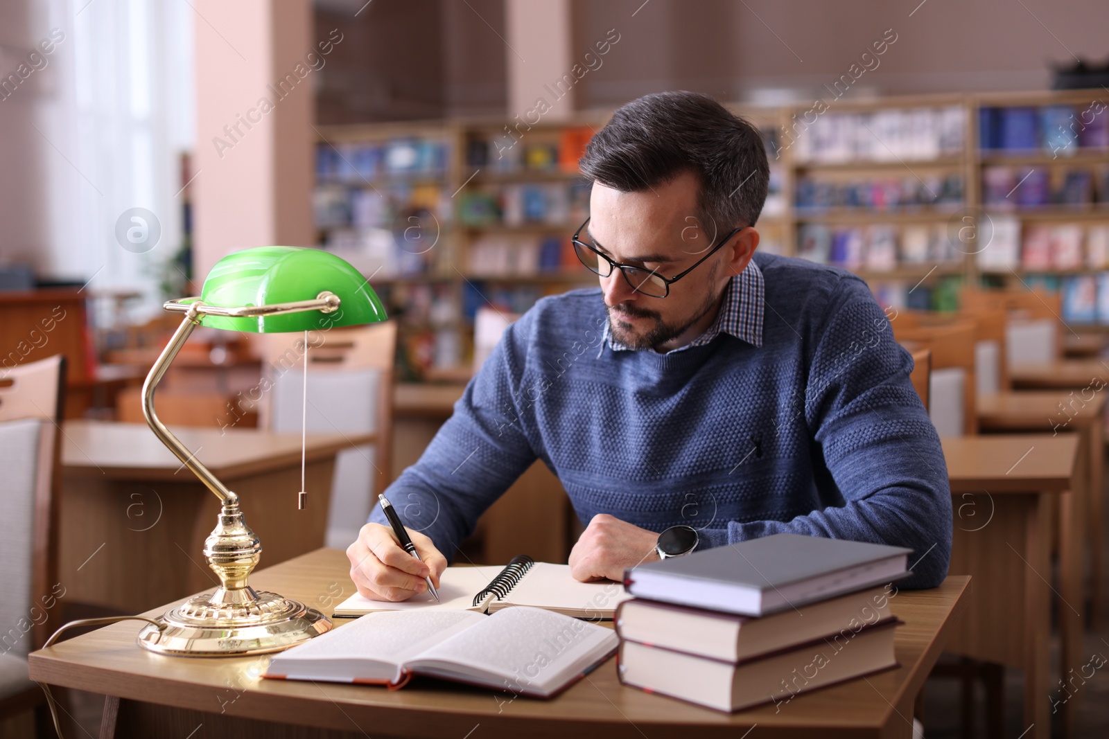 Photo of Handsome man reading book and taking notes at desk in library