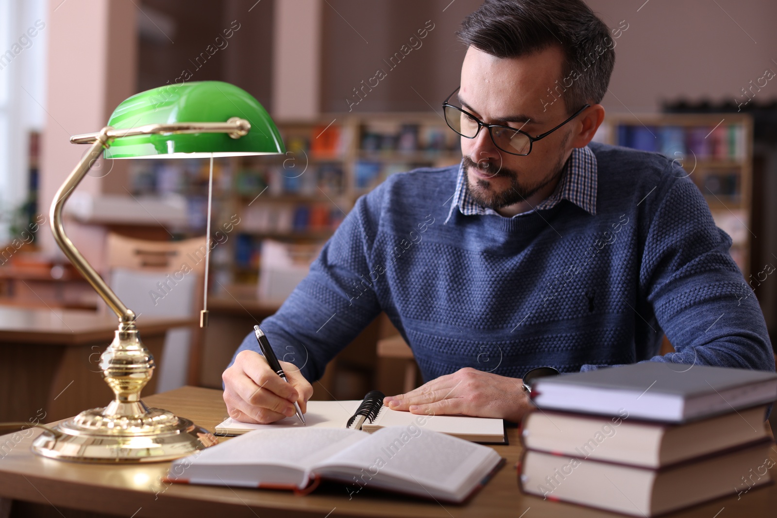 Photo of Handsome man reading book and taking notes at desk in library