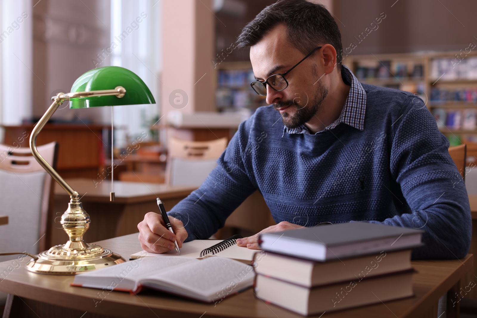 Photo of Handsome man reading book and taking notes at desk in library