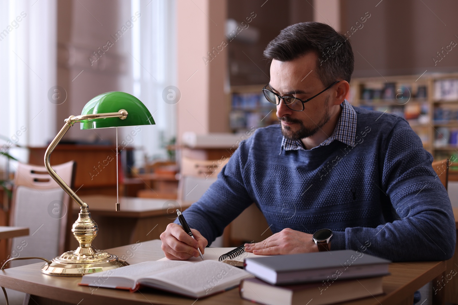 Photo of Handsome man reading book and taking notes at desk in library