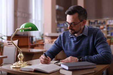 Photo of Handsome man reading book and taking notes at desk in library