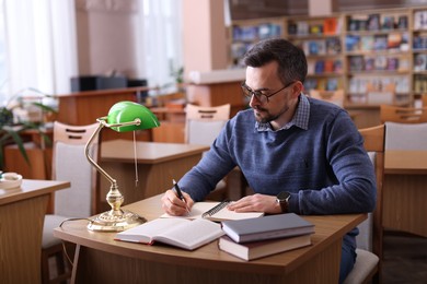 Photo of Handsome man reading book and taking notes at desk in library