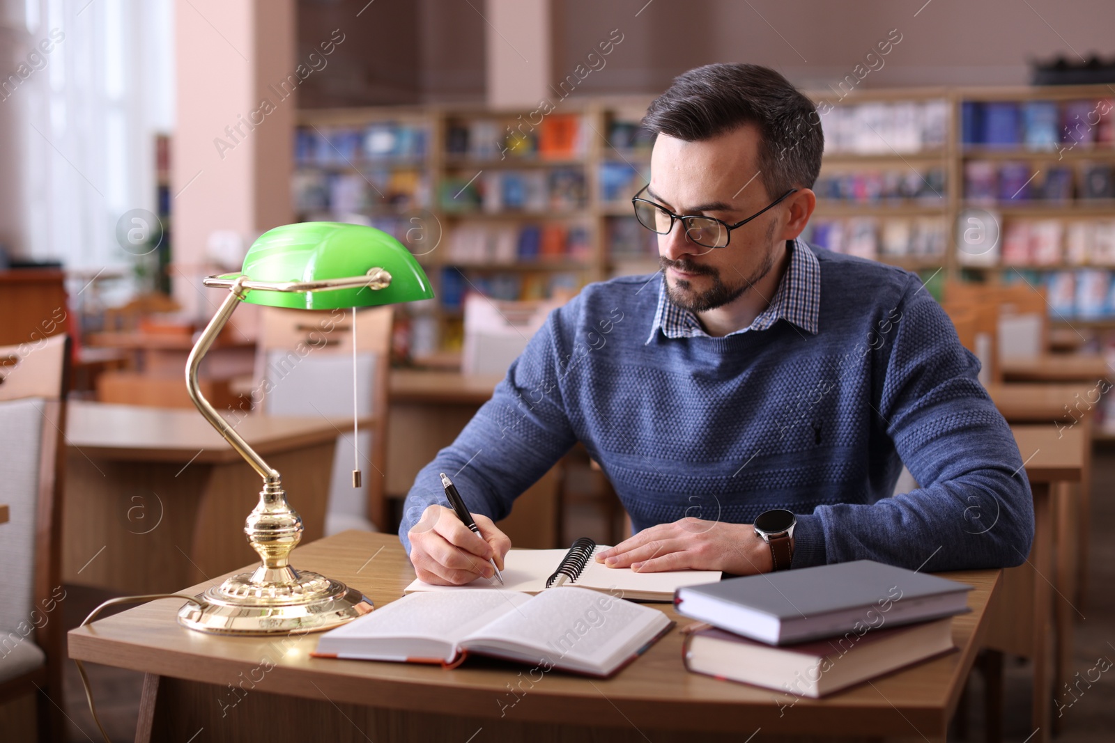 Photo of Handsome man reading book and taking notes at desk in library