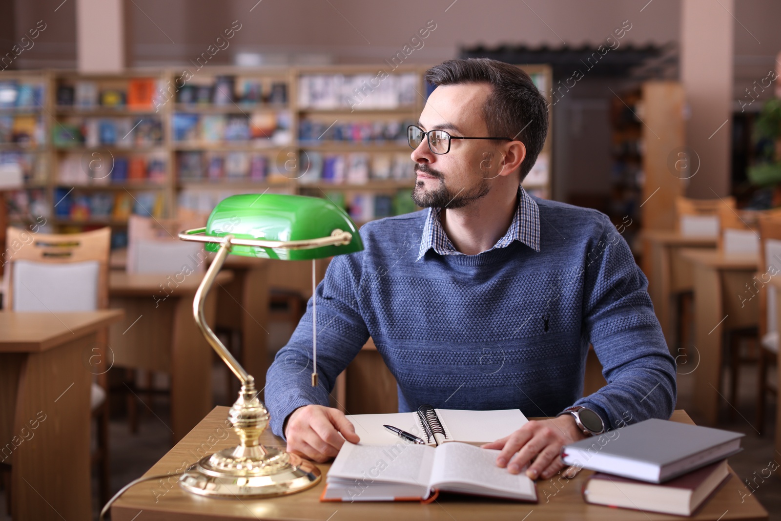 Photo of Handsome man with books at desk in library