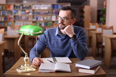 Photo of Handsome man with books at desk in library