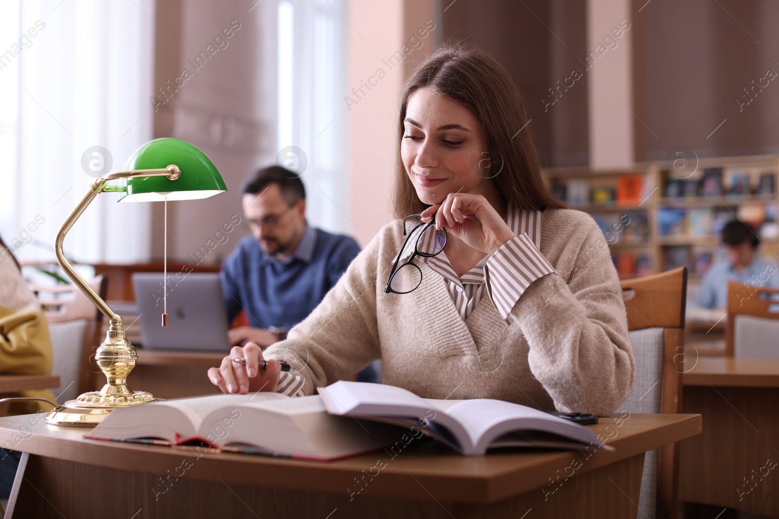 Photo of Beautiful woman reading book and taking notes at desk in public library