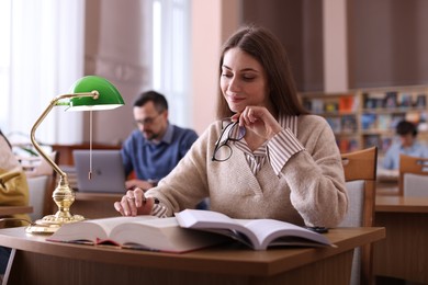 Beautiful woman reading book and taking notes at desk in public library