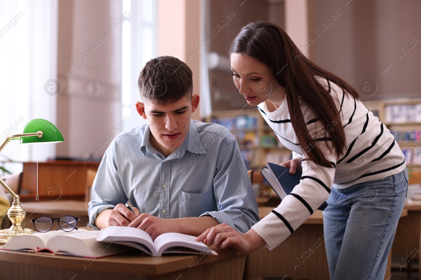 Photo of Woman pointing at something in book to her friend in library