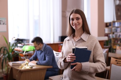 Portrait of smiling woman with books in library. Space for text