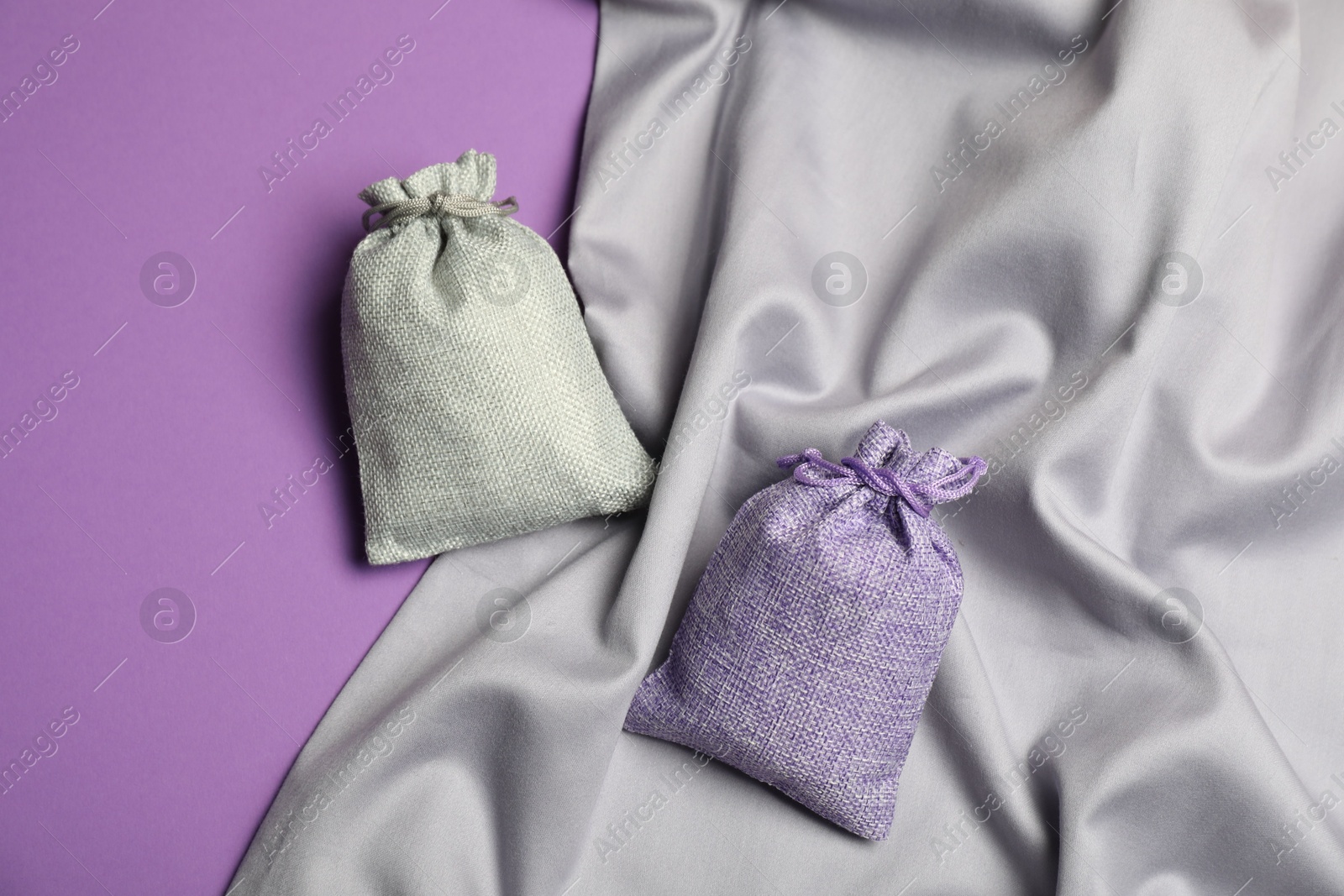 Photo of Burlap sacks and gray fabric on violet background, flat lay