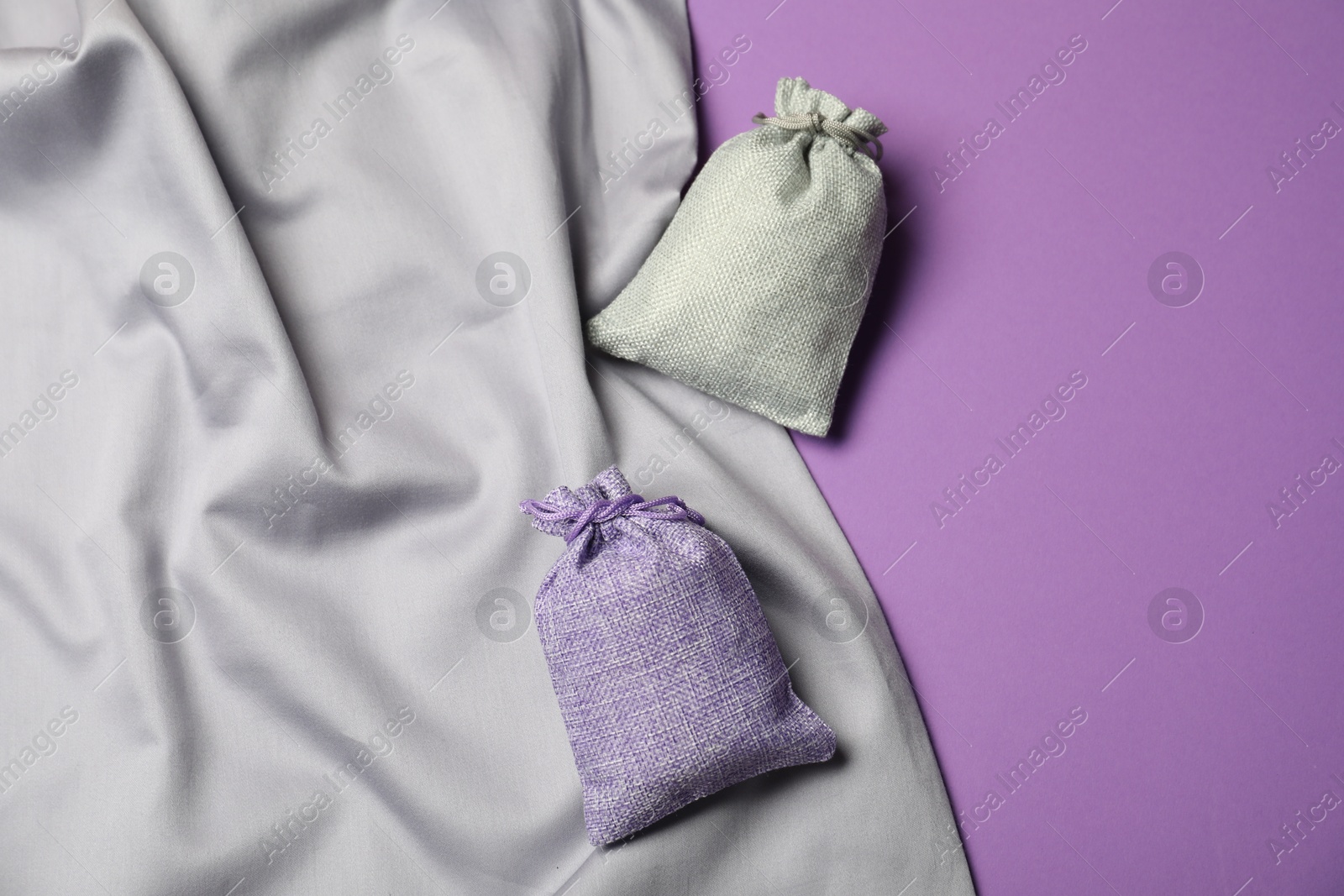 Photo of Burlap sacks and gray fabric on violet background, flat lay