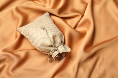 Photo of Beige burlap sack on orange fabric, above view. Space for text