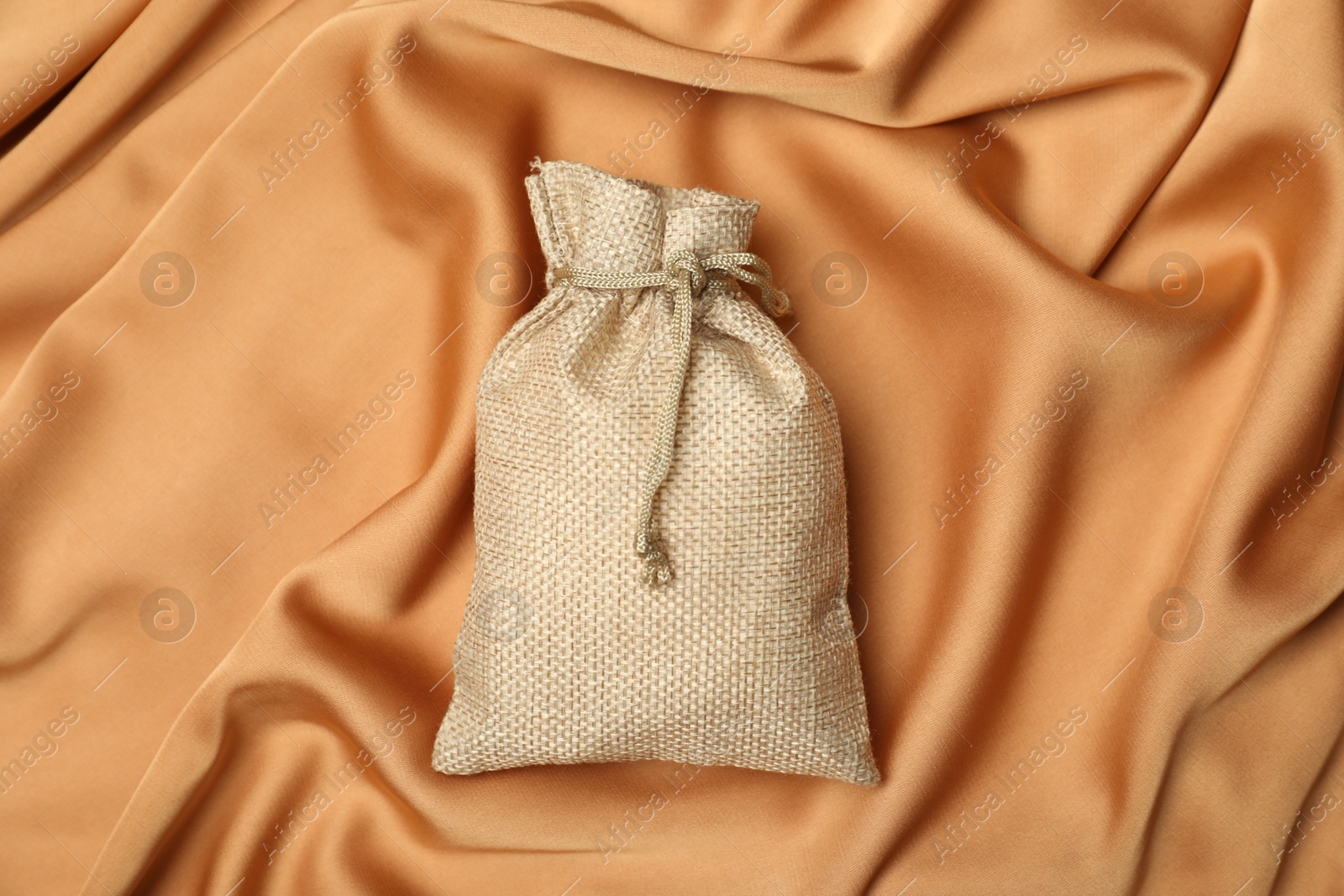 Photo of Beige burlap sack on orange fabric, top view