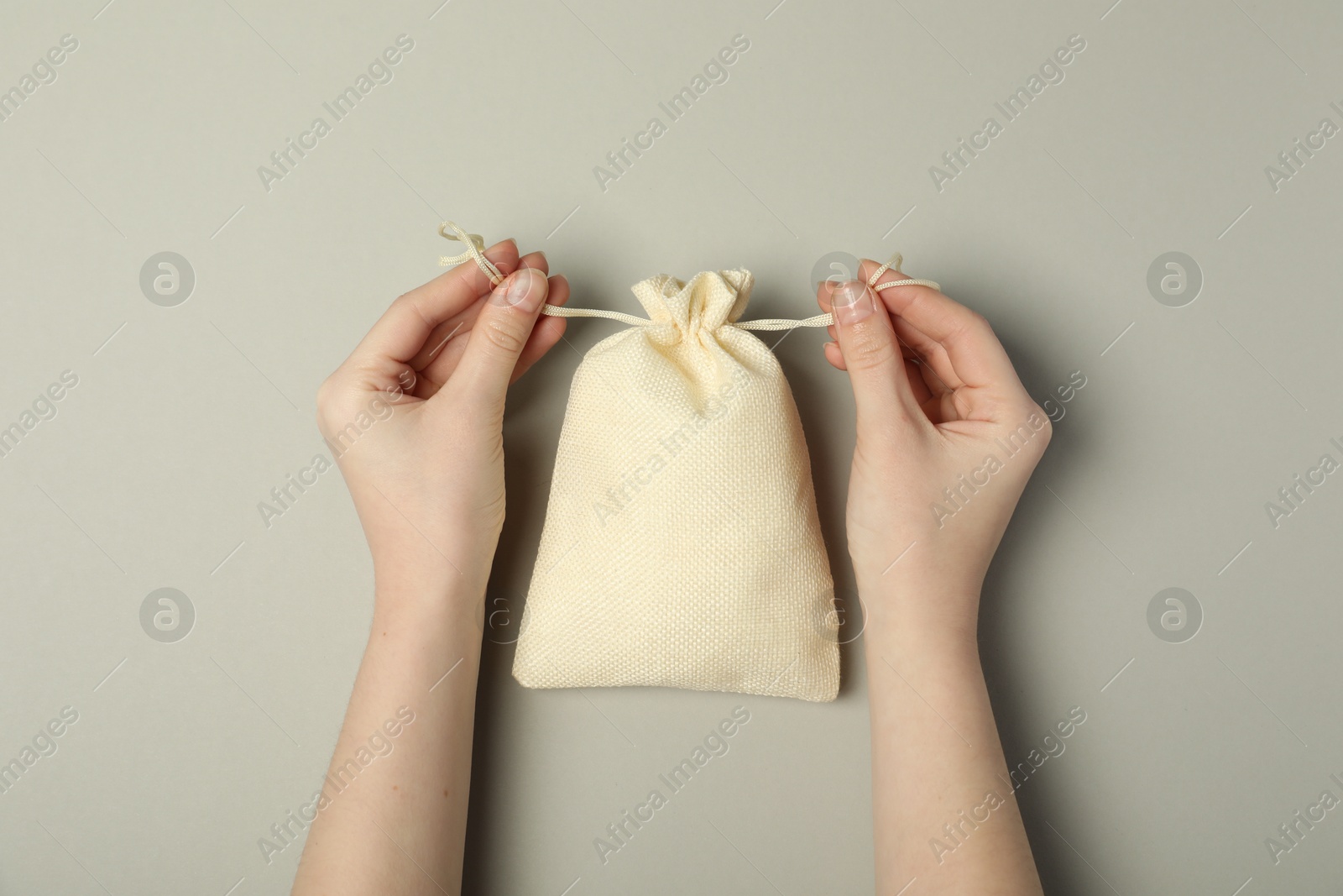 Photo of Woman with beige burlap sack on gray background, top view