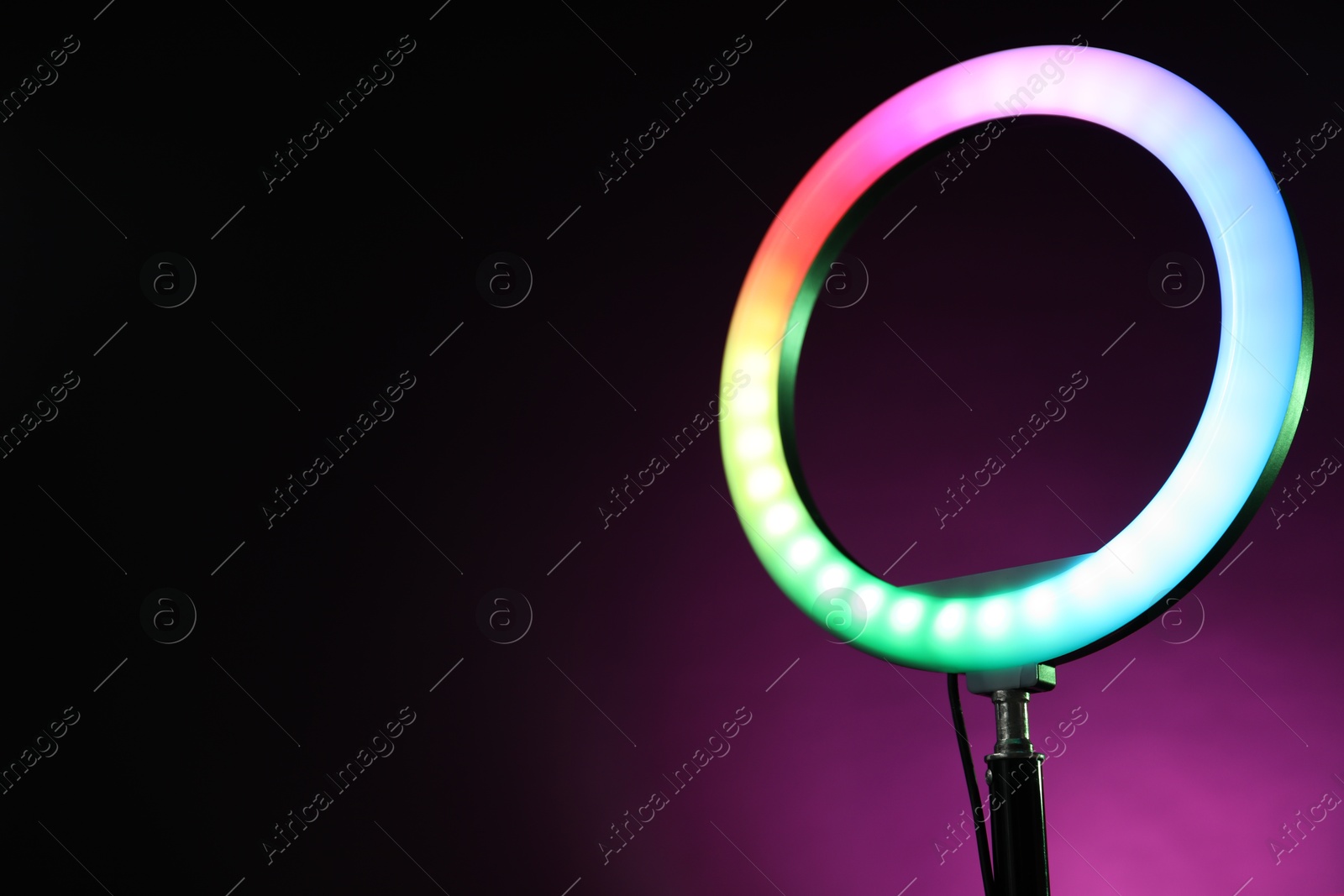 Photo of Ring lamp on stand against dark purple background, closeup. Space for text