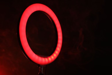 Photo of Ring lamp on stand against dark red background in smoke, closeup. Space for text