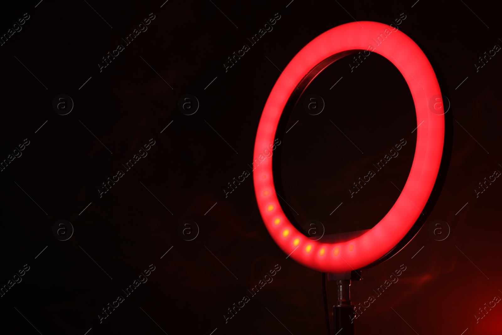 Photo of Ring lamp on stand against dark red background in smoke, closeup. Space for text