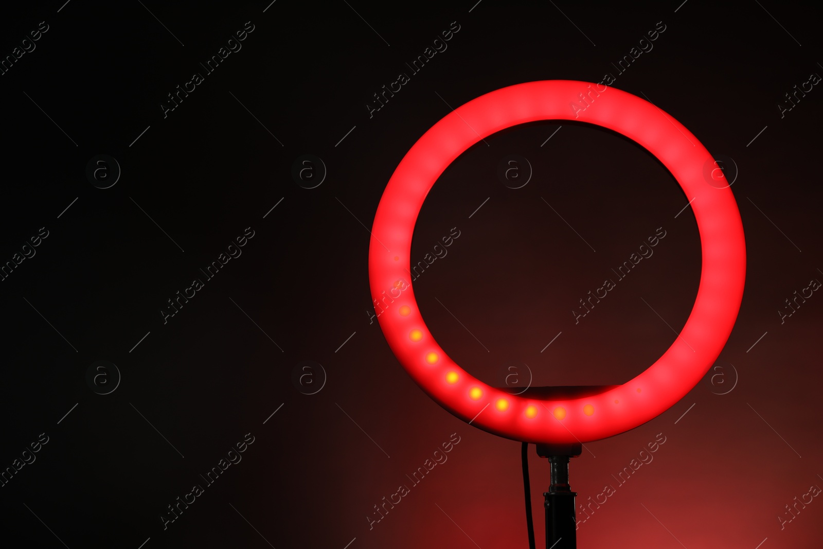 Photo of Ring lamp on stand against dark red background, space for text