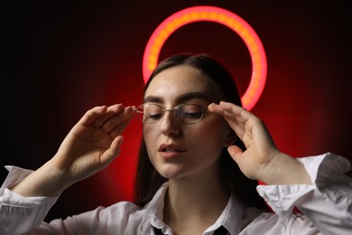 Photo of Beautiful woman with ring lamp wearing glasses on dark red background