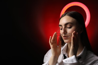 Photo of Beautiful woman with ring lamp wearing glasses on dark red background, space for text