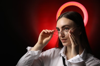 Photo of Beautiful woman with ring lamp wearing glasses on dark red background, space for text