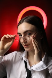 Photo of Beautiful woman with ring lamp wearing glasses on dark red background