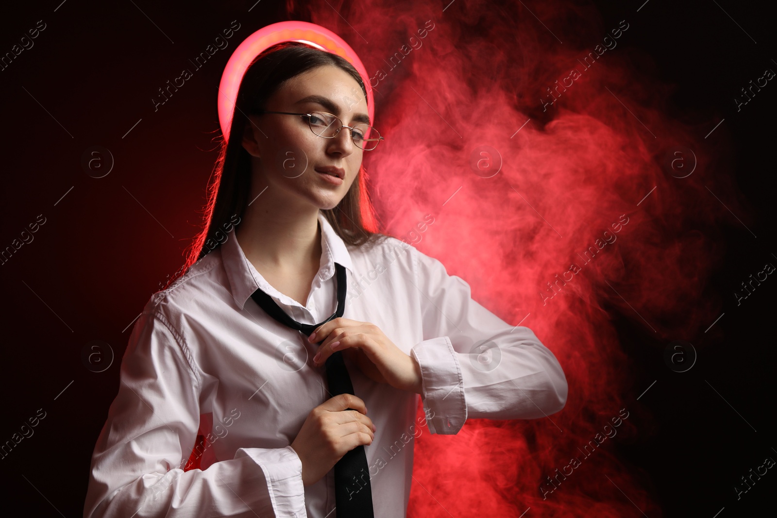 Photo of Beautiful woman with ring lamp adjusting necktie on dark red background in smoke, space for text