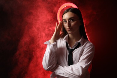 Photo of Beautiful woman with ring lamp wearing glasses on dark red background in smoke, space for text