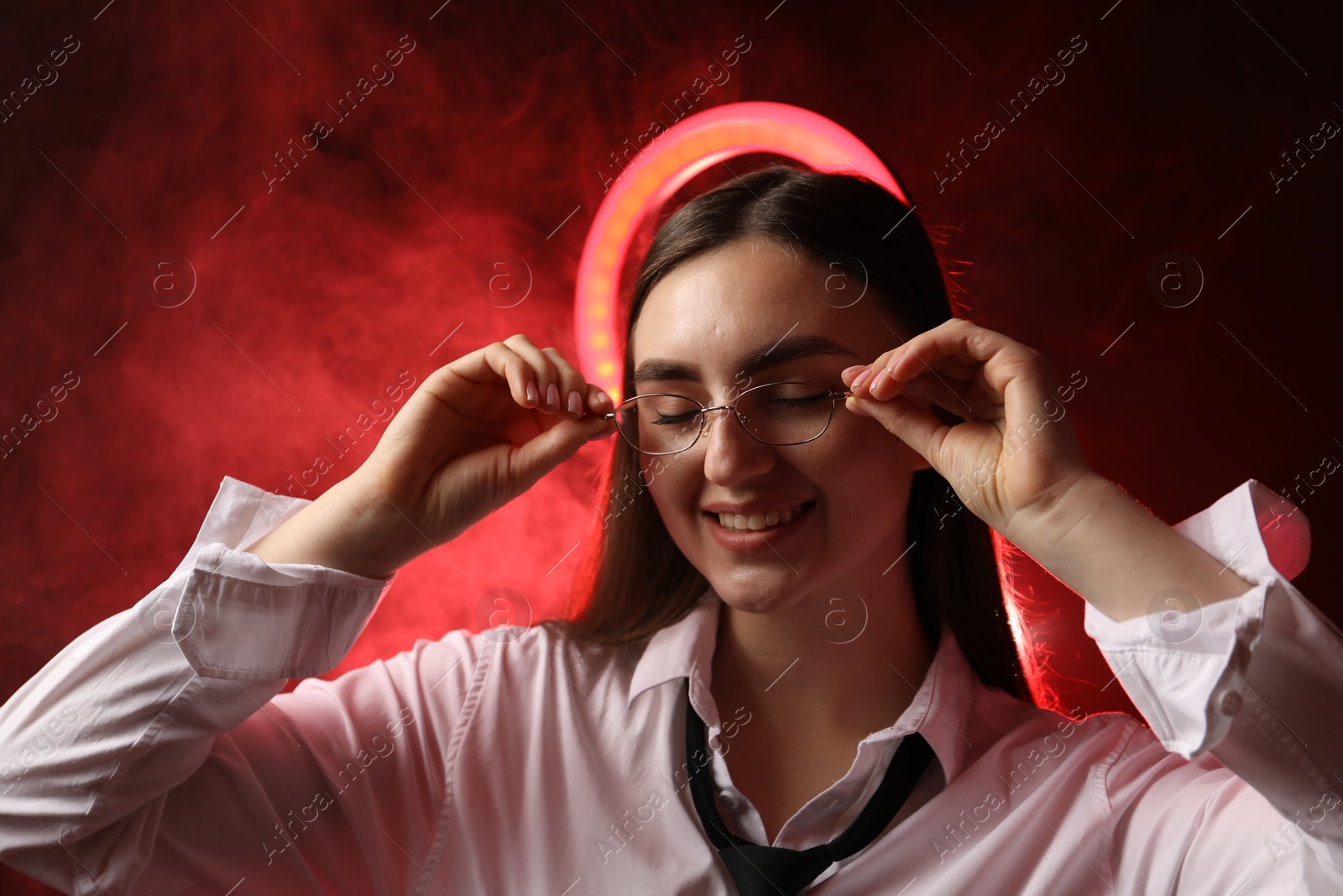 Photo of Beautiful woman with ring lamp wearing glasses on dark red background in smoke