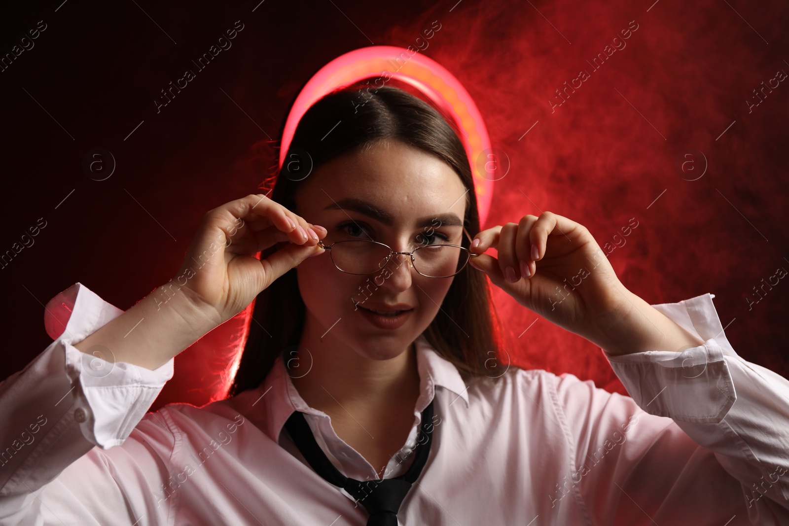 Photo of Beautiful woman with ring lamp wearing glasses on dark red background in smoke