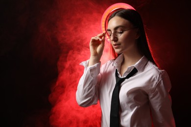 Photo of Beautiful woman with ring lamp wearing glasses on dark red background in smoke, space for text