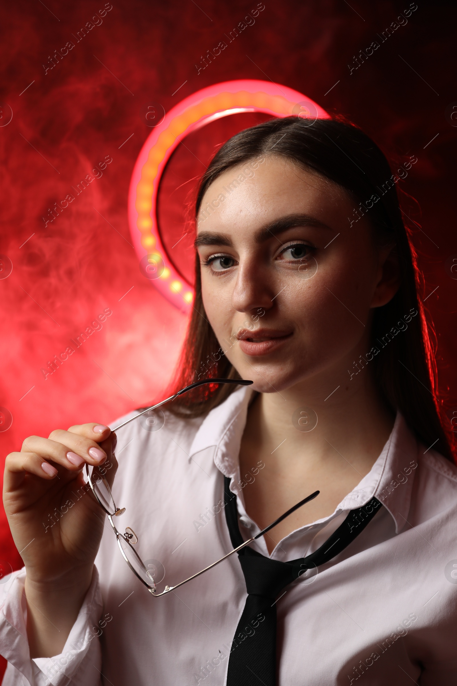 Photo of Beautiful woman with ring lamp and glasses on dark red background in smoke